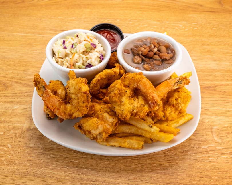 Fried shrimp and french fries with sides of coleslaw, baked beans, and ketchup on a white plate.