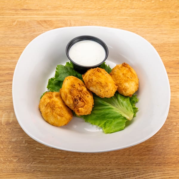 Four golden-brown fried cheese curds on lettuce with a side of ranch dressing on a white plate.