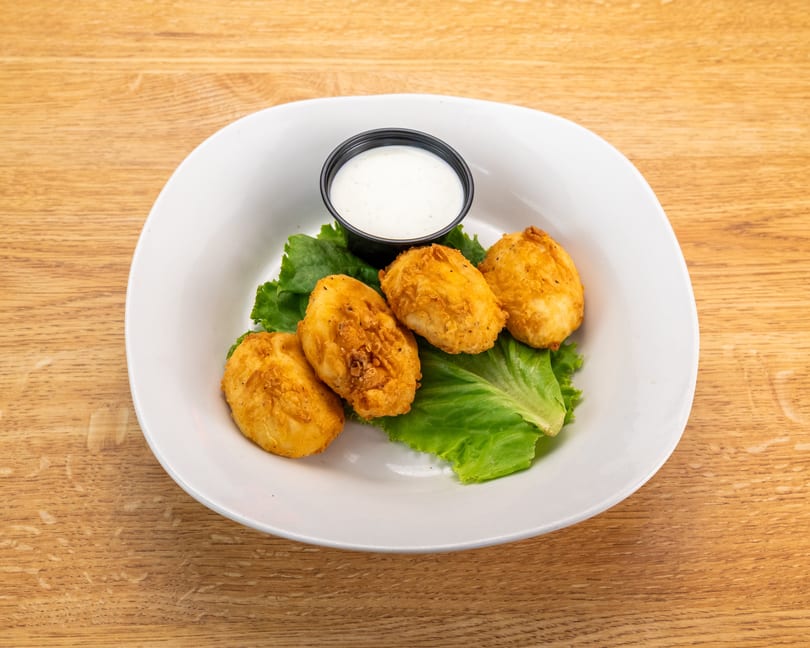 Four golden-brown fried cheese curds on lettuce with a side of ranch dressing on a white plate.