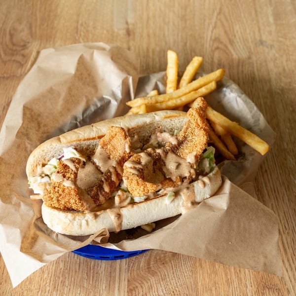 Fried shrimp po'boy sandwich with coleslaw and sauce, served with french fries on a wooden table.