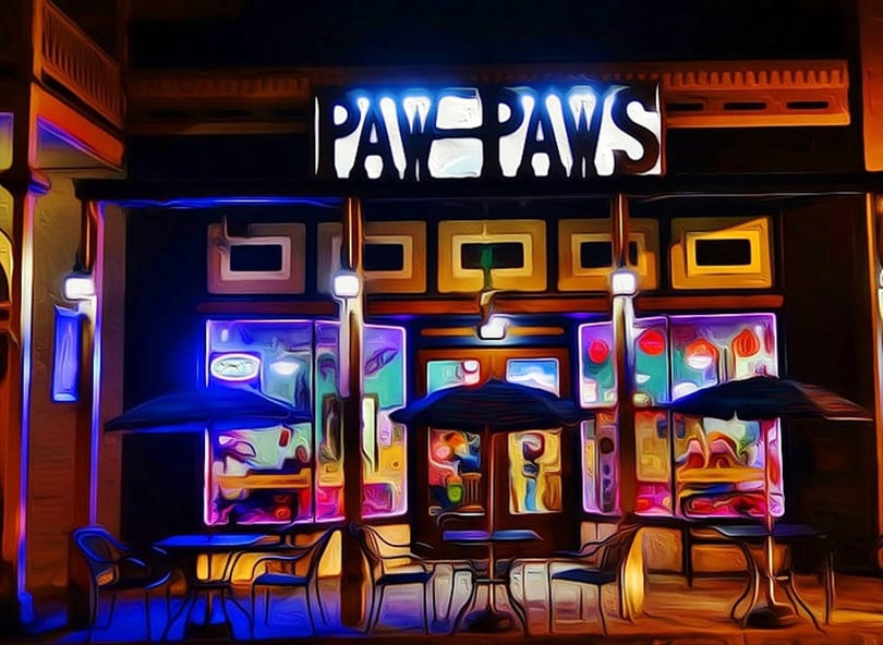 Vibrant, neon-lit "Paw Paws" restaurant exterior at night with outdoor seating and umbrellas.