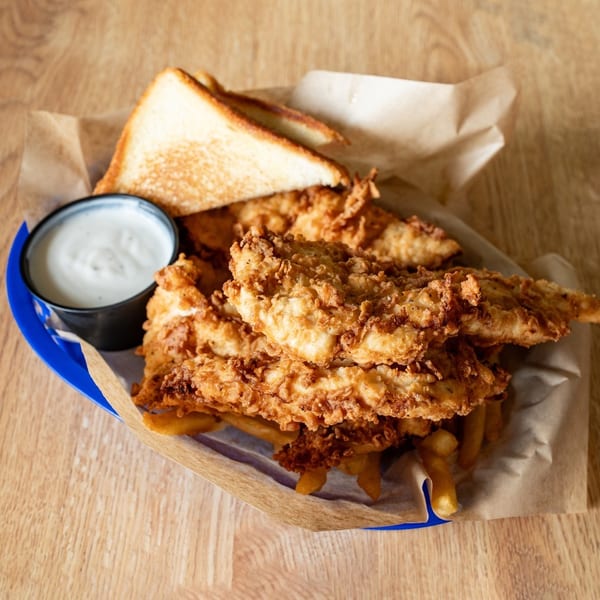 Crispy fried chicken tenders, french fries, Texas toast, and ranch dip in a blue basket.