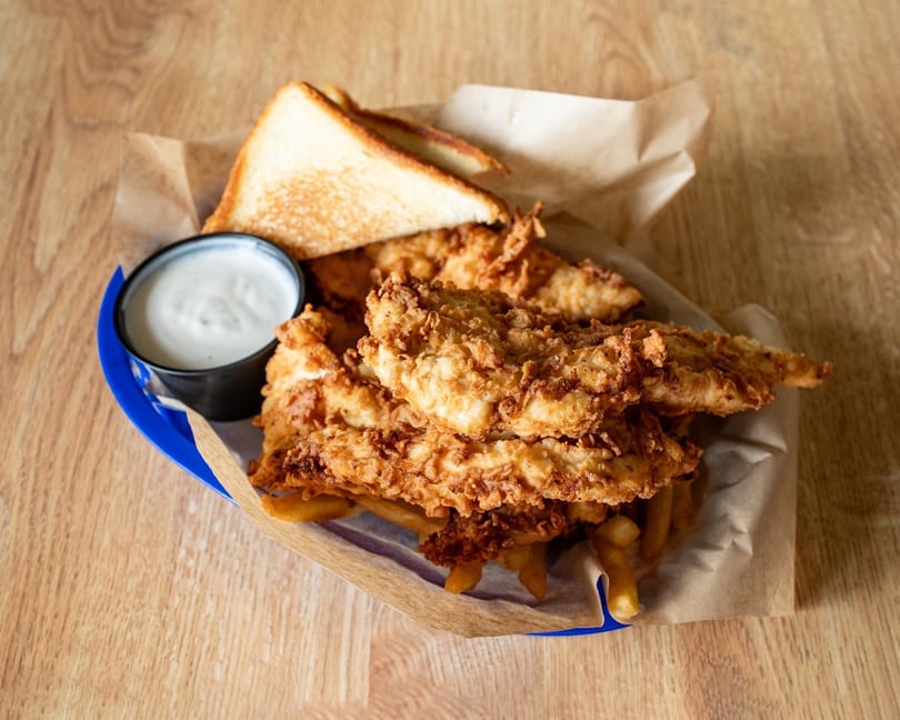 Crispy fried chicken tenders, french fries, Texas toast, and ranch dip in a blue basket.