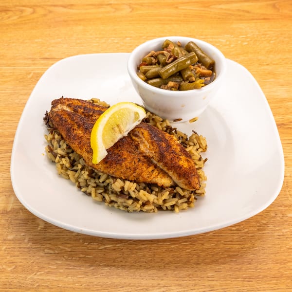 Blackened fish fillets with a lemon wedge, wild rice, and a side of green beans.