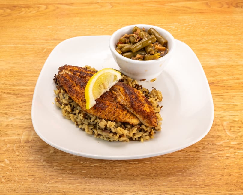 Blackened fish fillets with a lemon wedge, wild rice, and a side of green beans.